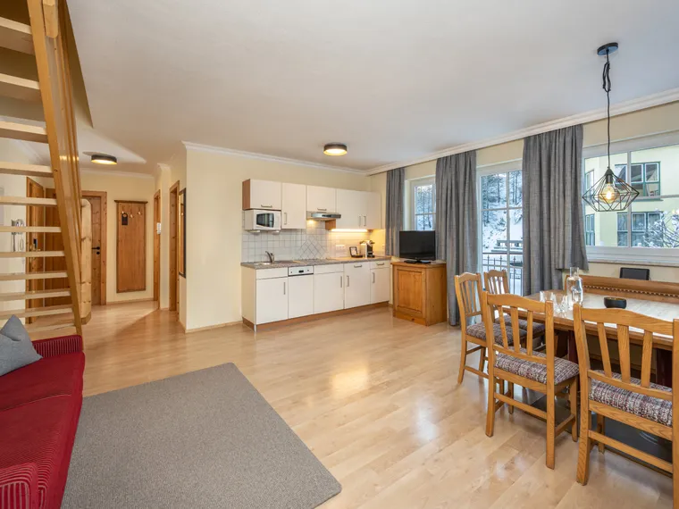 Cozy holiday apartment with open kitchen, wooden dining area, sofa, and stairs to upper level