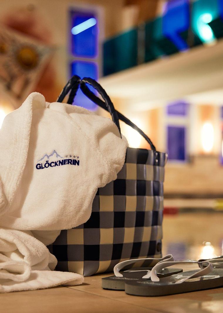 Wellness-Bademantel mit Glocknerin-Logo neben Korb und Flip-Flops am Innenpool