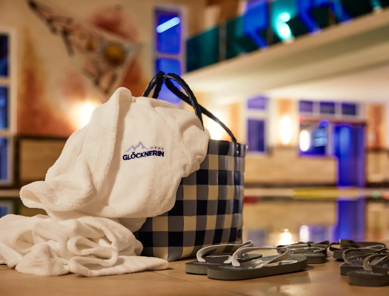 Wellness-Bademantel mit Glocknerin-Logo neben Korb und Flip-Flops am Innenpool