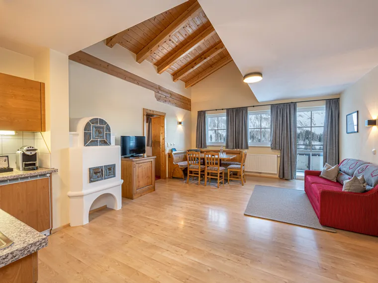 Cozy alpine apartment with wooden ceiling, red sofa, dining area, and mountain view