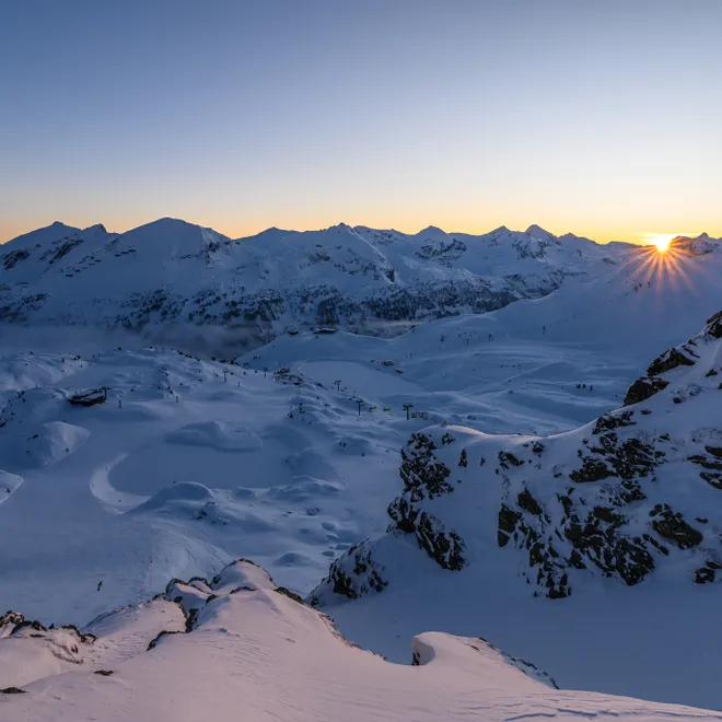 Winter sunrise over snow-covered alpine mountains and ski slopes