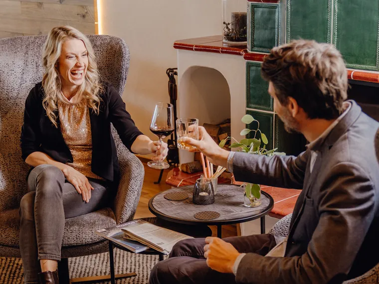 Fröhliches Paar stößt mit Wein in gemütlicher Lounge mit stilvoller Einrichtung an