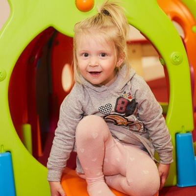 Toddler girl playing inside colorful caterpillar play tunnel at daycare
