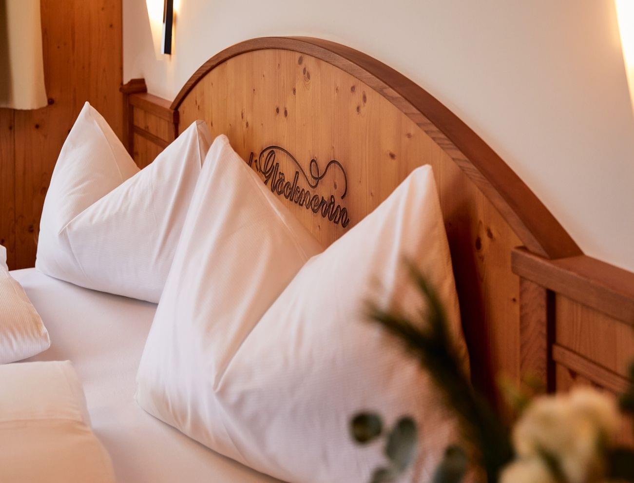Cozy hotel bed with white pillows and wooden headboard reading Glocknerin