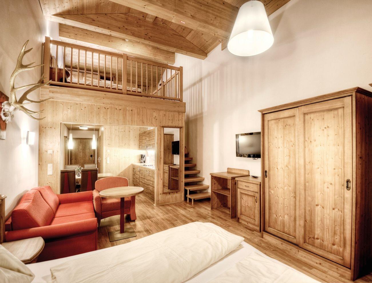 Gemütliches Alpenhotelzimmer mit Holzmöbeln, Schlafboden und rotem Sofa