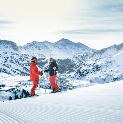 Two skiers on freshly groomed slope in snowy alpine mountain landscape