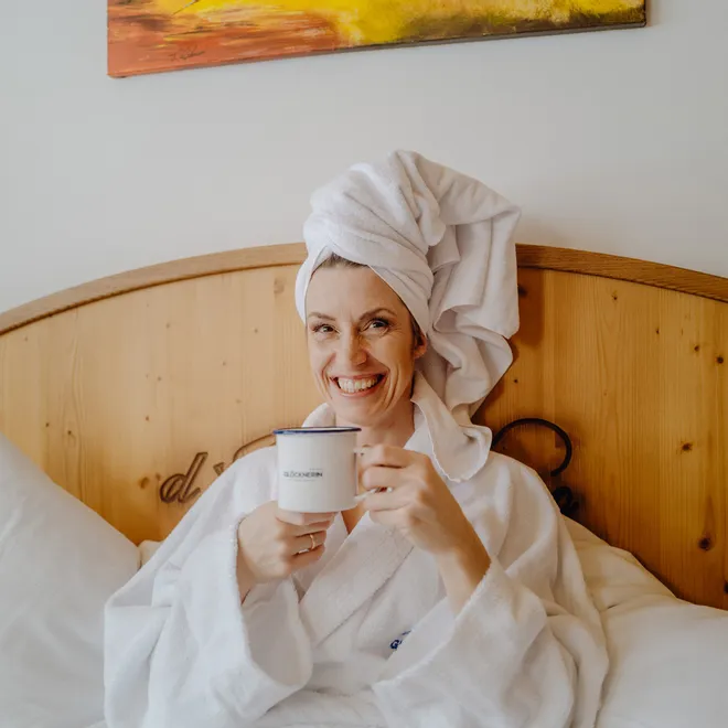 Smiling woman in bathrobe holding coffee mug in hotel bed
