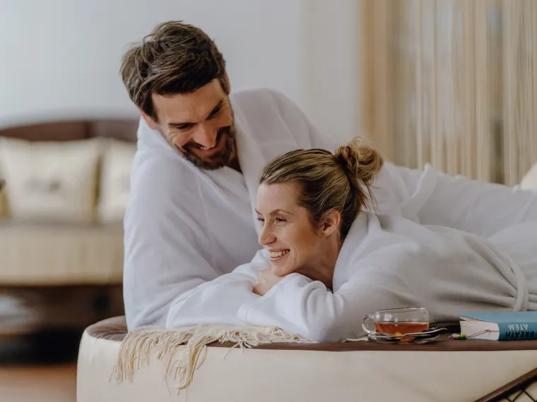 Couple in white bathrobes relaxing at spa with tea and book on side