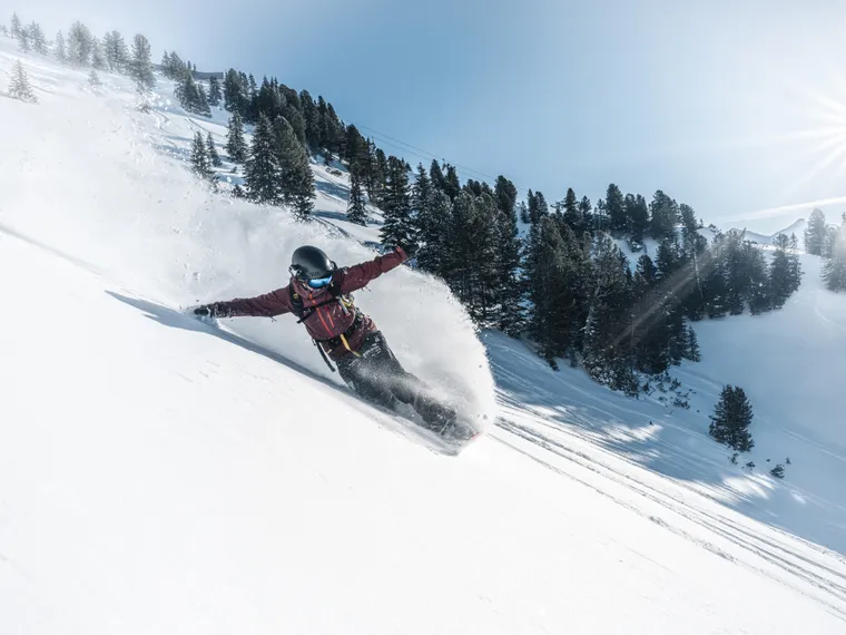 Snowboarder carving through fresh powder on a sunny mountain slope