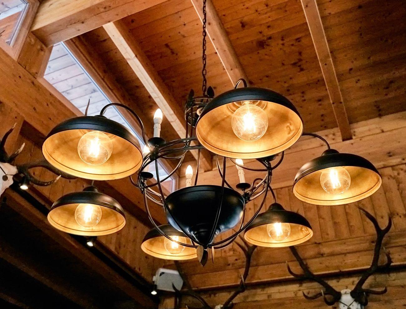 Rustic chandelier with exposed bulbs hanging from wooden ceiling with antlers