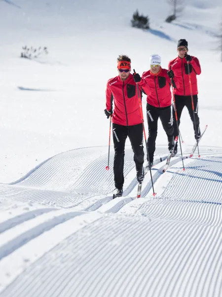 Three cross-country skiers in red jackets gliding on groomed snow trail
