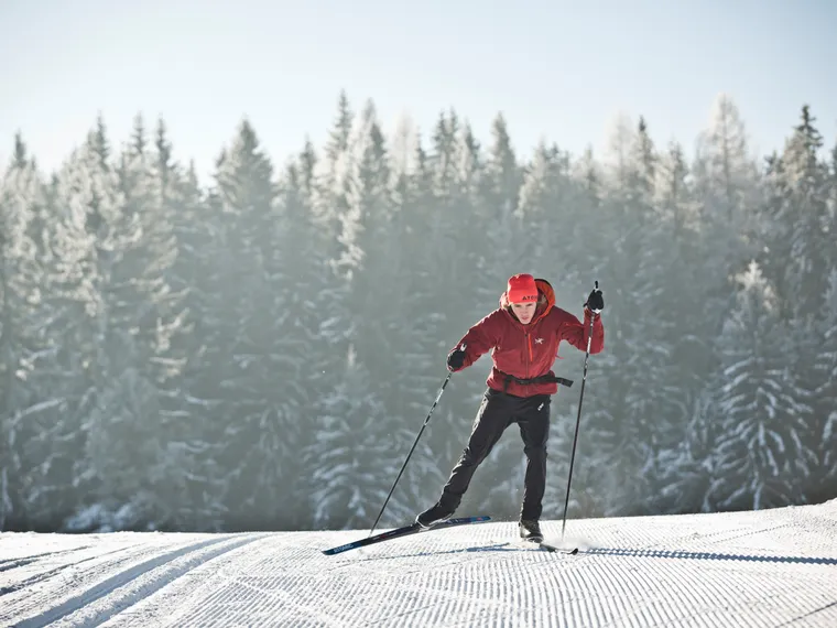 Cross-country skier in red gear gliding on snowy trail through winter forest