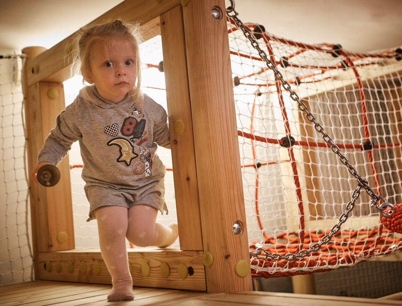 Kleines Kind spielt in einem Indoor-Kletterparcours mit Holzstruktur und Netzen