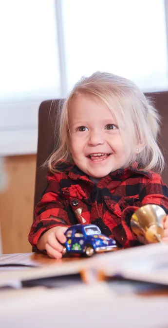 Smiling toddler playing with toy car and bell at the table