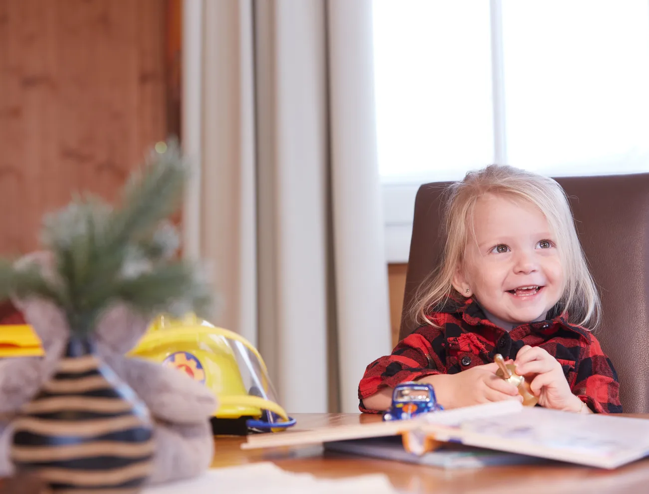 Lächelndes kleines Mädchen am Tisch mit Spielzeug und Kinderbuch