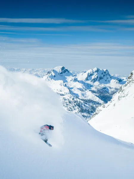 Skier carving through deep powder snow in alpine mountain landscape