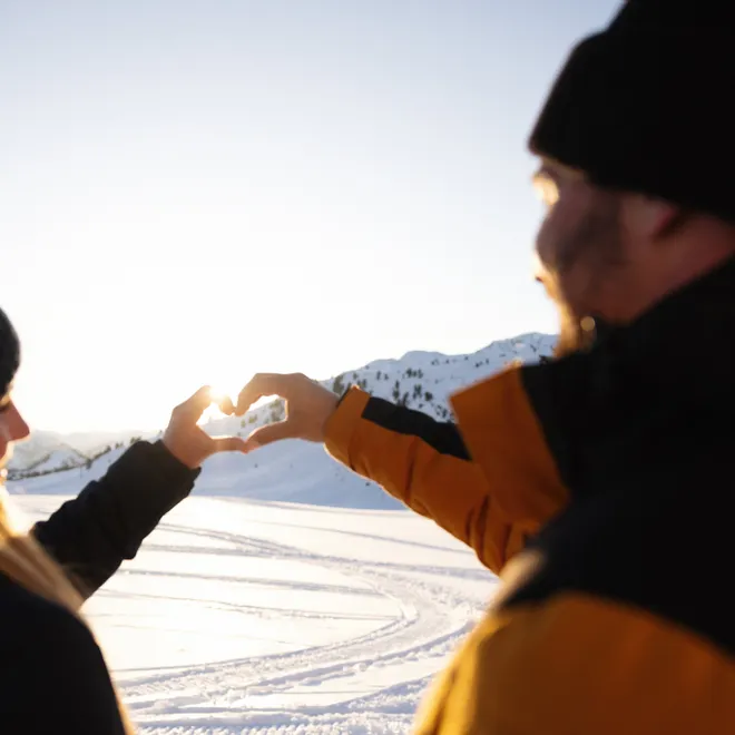 Couple making heart shape with hands against snowy mountain sunset