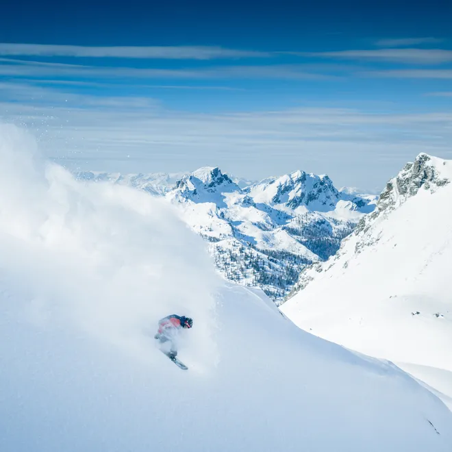 Skier carving through deep powder snow in alpine mountain landscape
