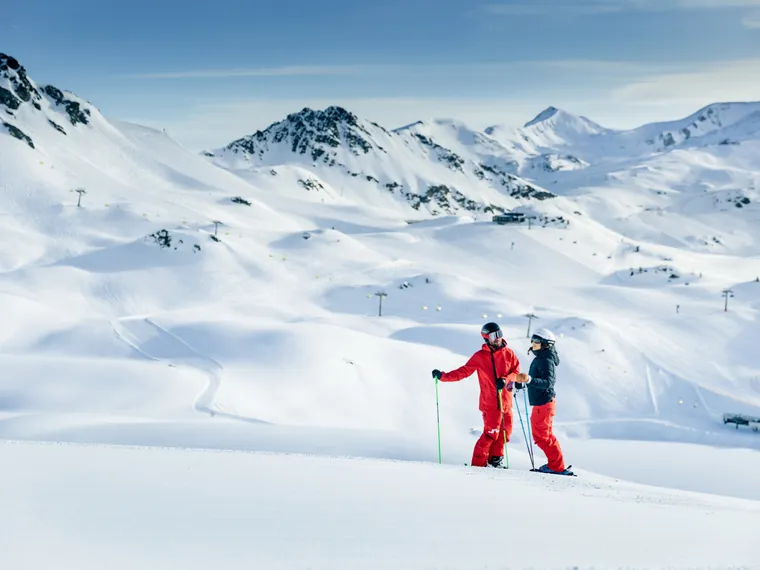 Two skiers in red outfits standing on ski slope in snowy alpine mountains