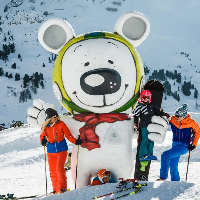 Family posing by giant bear mascot statue at snowy ski resort