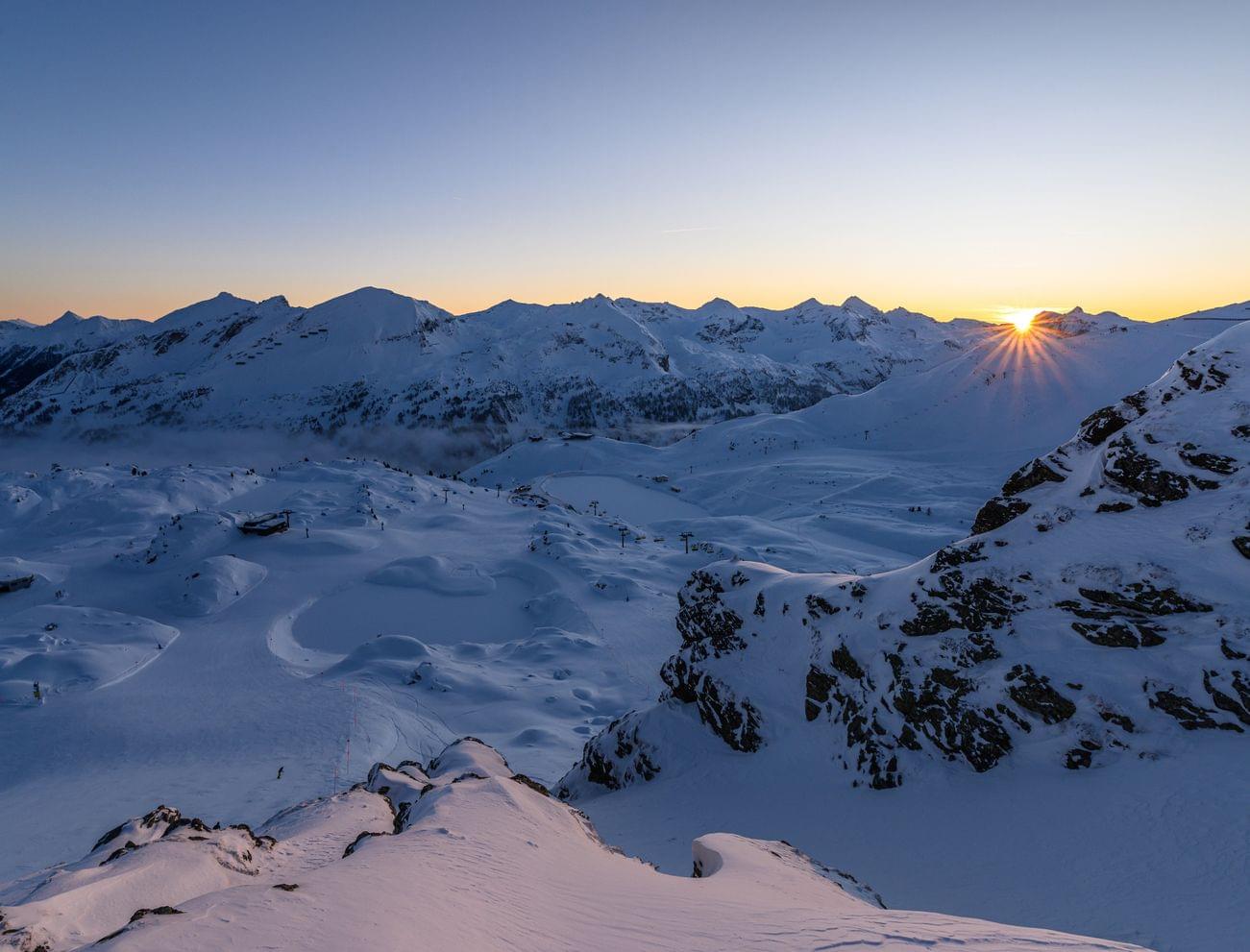 Winterlicher Sonnenaufgang über schneebedeckten Alpen und Skipisten