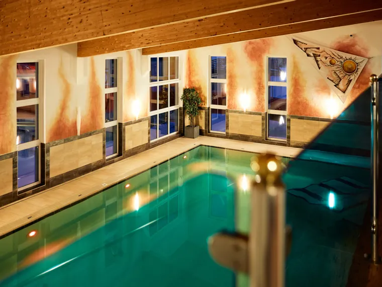 Beleuchteter Innenpool mit Holzdecke und Wandmalerei in warmen Farben