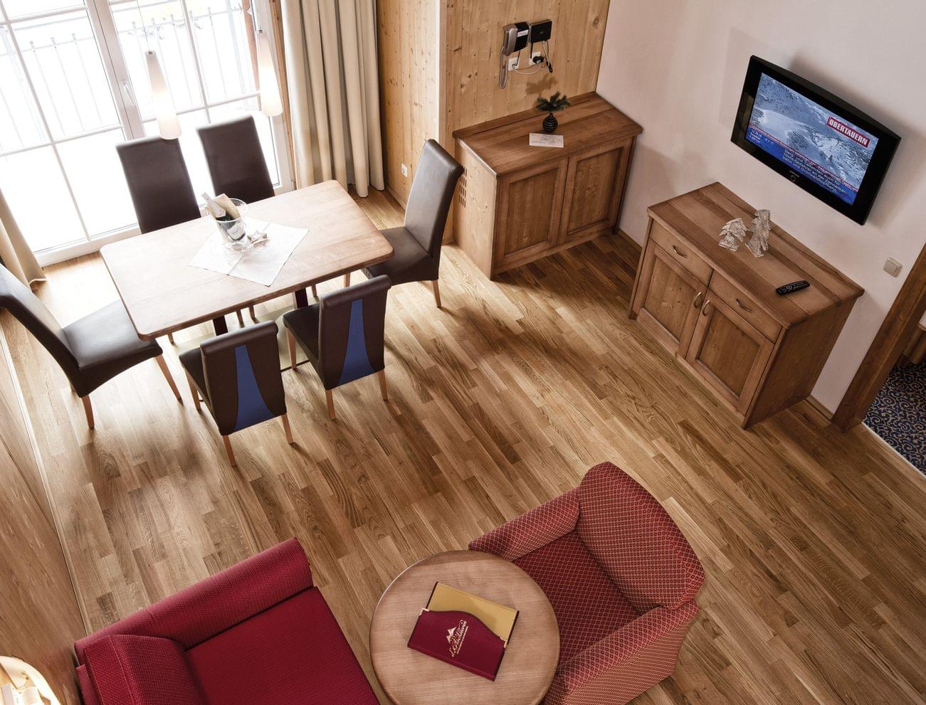Gemütliches Hotelzimmer mit Holzmöbeln, Esstisch, Sesseln und wandmontiertem Fernseher