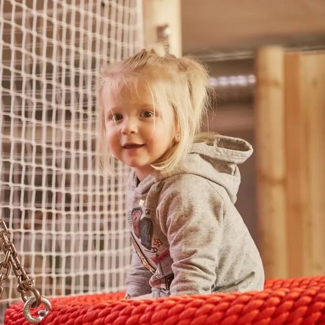 Kleines Mädchen auf einer roten Nestschaukel in einem Indoor-Spielplatz