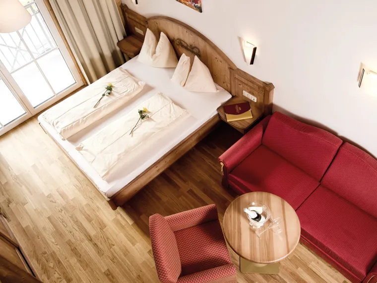 Cozy hotel room with double bed, red sofa, wooden floor and natural light