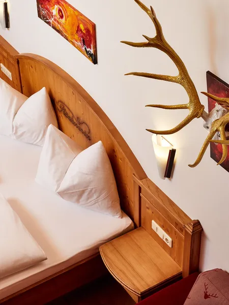 Gemütliches Hotelzimmer mit Doppelbett, Holz-Kopfteil, Geweihdeko und moderner Wandbeleuchtung