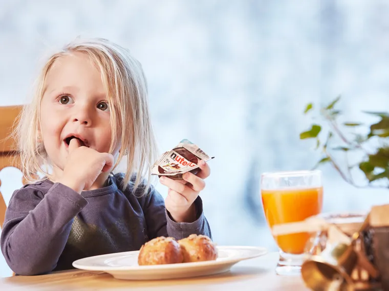 Kind isst Nutella mit Brötchen zum Frühstück mit Orangensaft