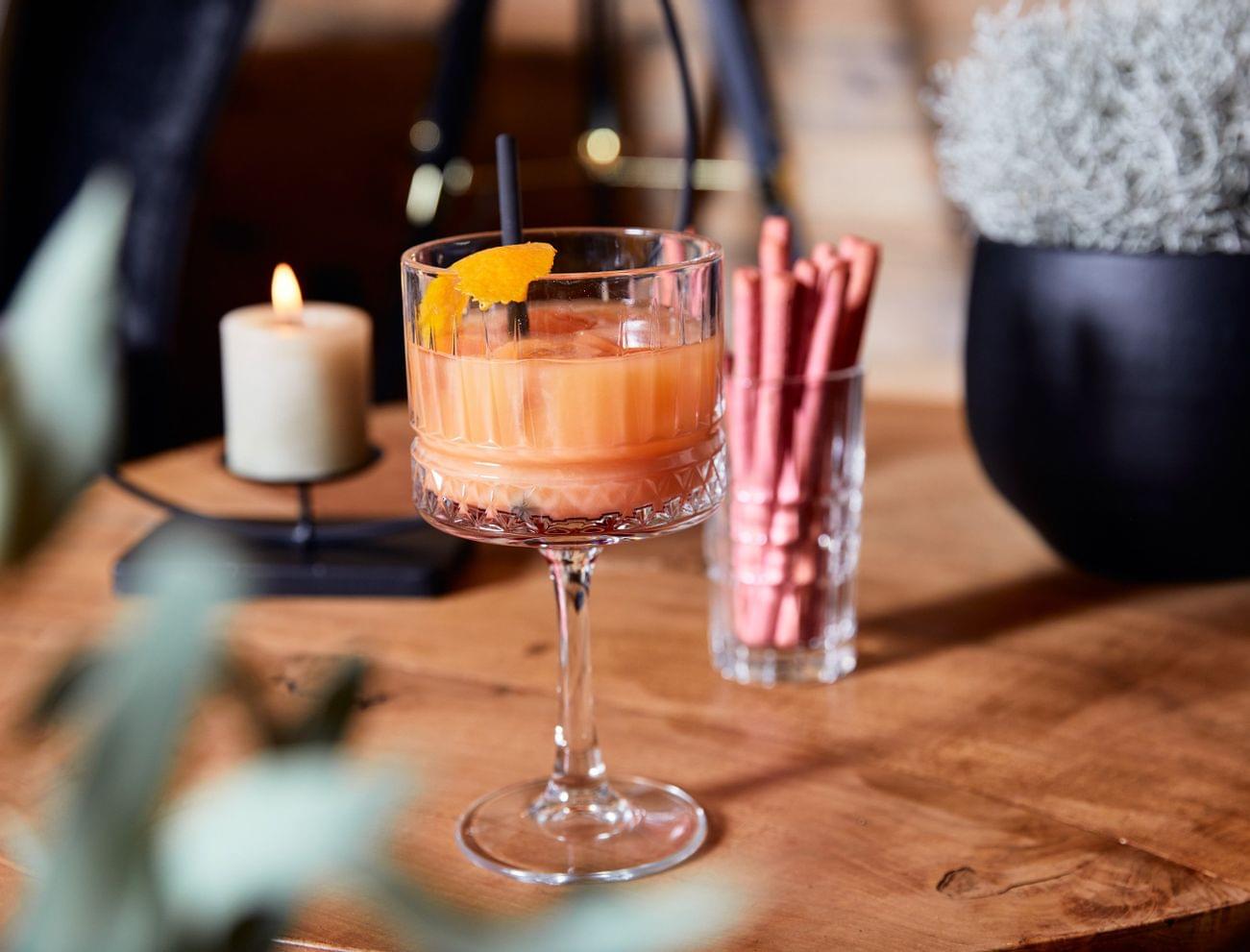 Serviertes Cocktailglas mit Orangendrink und Eiswürfeln auf einem Holztisch