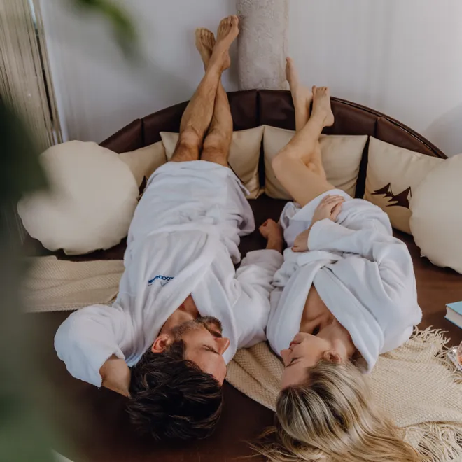 Couple in white bathrobes relaxing on round spa lounge bed